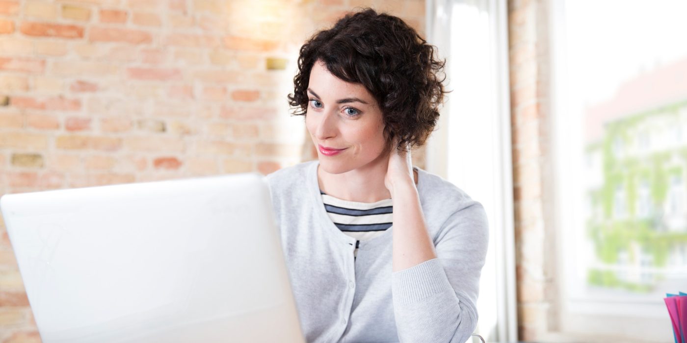 Woman looking at computer screen in front of brick-lined wall